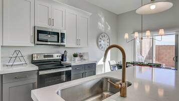 A modern kitchen with white cabinetry, stainless steel appliances, and a large island with a gold faucet.