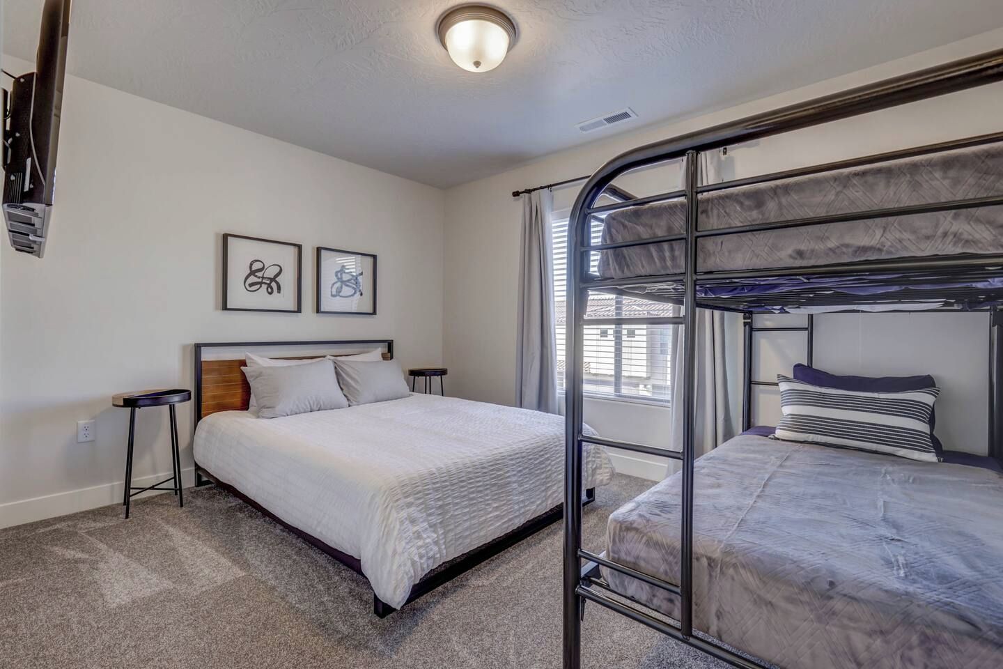A room with a bunk bed, a single bed, a small stool, and two framed pictures on the wall.