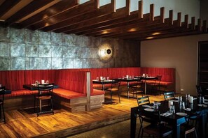 En restaurantindretning med trægulv, rødt polstrede siddepladser og bordopstilling til spisning.