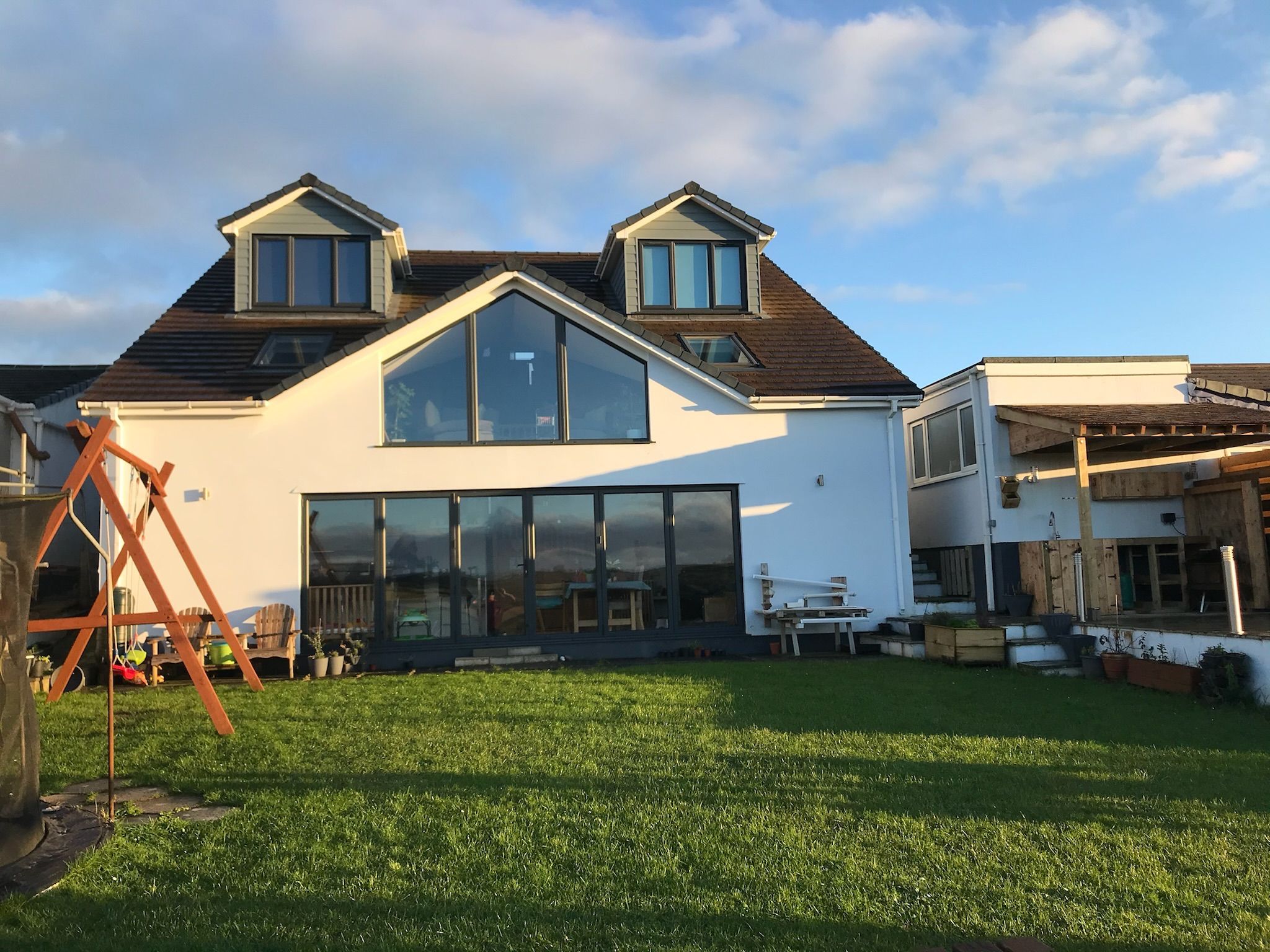 Une maison moderne à deux étages, dotée de grandes fenêtres et d’un toit en pente.