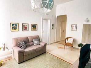 Una sala de estar con sofá, sillón, televisor y obras de arte enmarcadas en la pared.