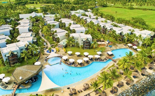 Et resort med flere bygninger, en stor swimmingpool og palmer.