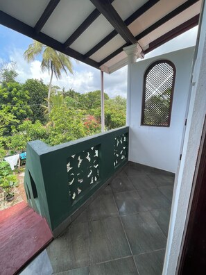 Ein überdachter Balkon mit Blick auf Grünflächen und einem Fliesenboden.