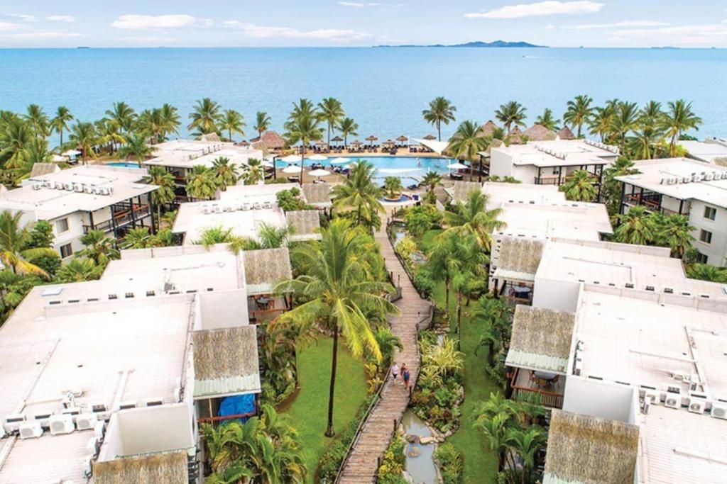 Un resort con varias edificaciones, una piscina central y vista al mar.