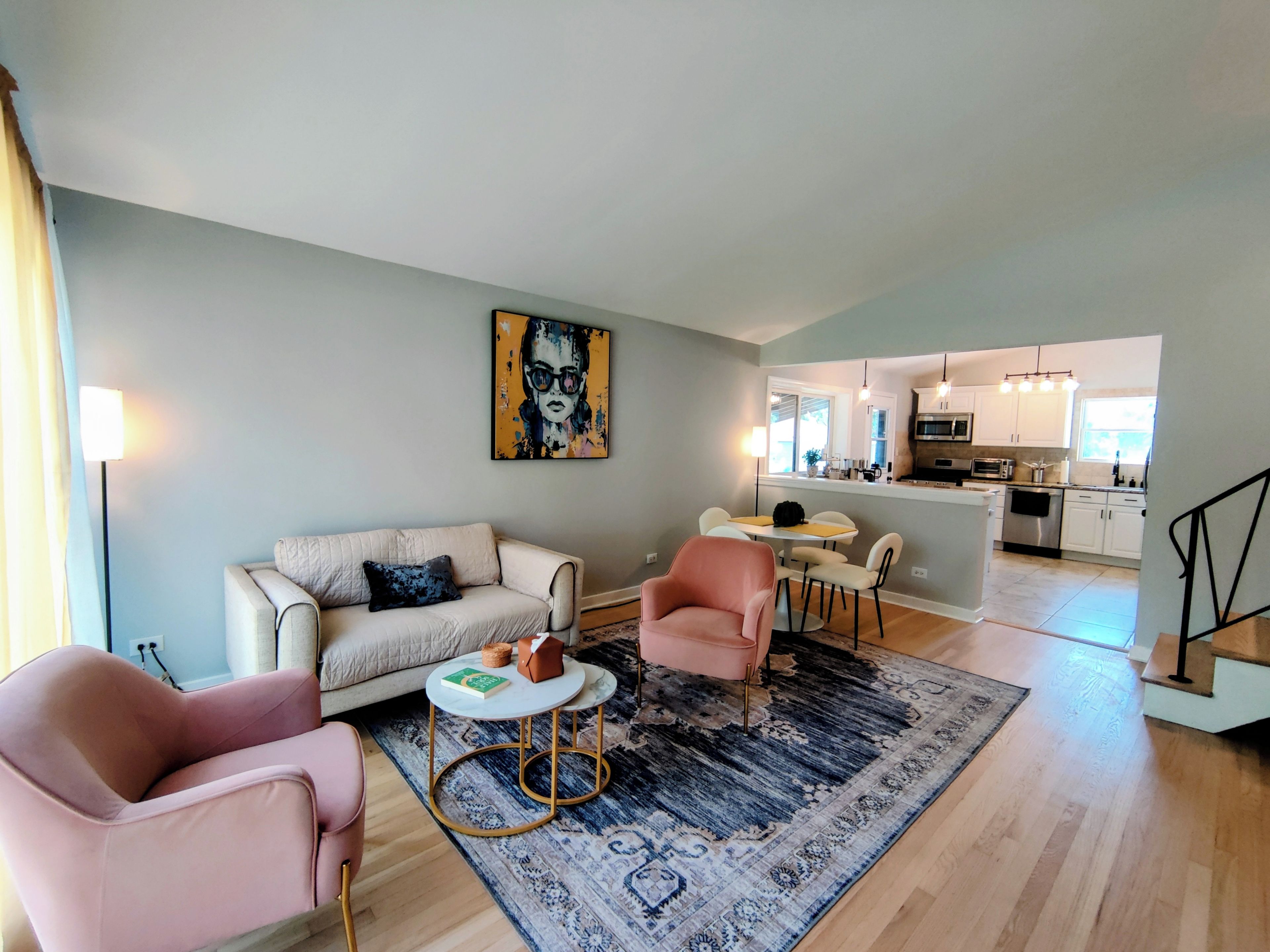 A modern living room with a sofa, armchairs, a coffee table, and a rug. A dining area with a table and chairs is visible in the background.