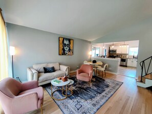 Een moderne woonkamer met een bank, fauteuils, een salontafel en een vloerkleed. In de achtergrond is een eethoek met een tafel en stoelen zichtbaar.