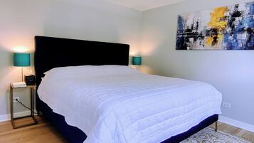 A bedroom with a large bed, two bedside lamps, a nightstand, a wall painting, and a patterned rug.