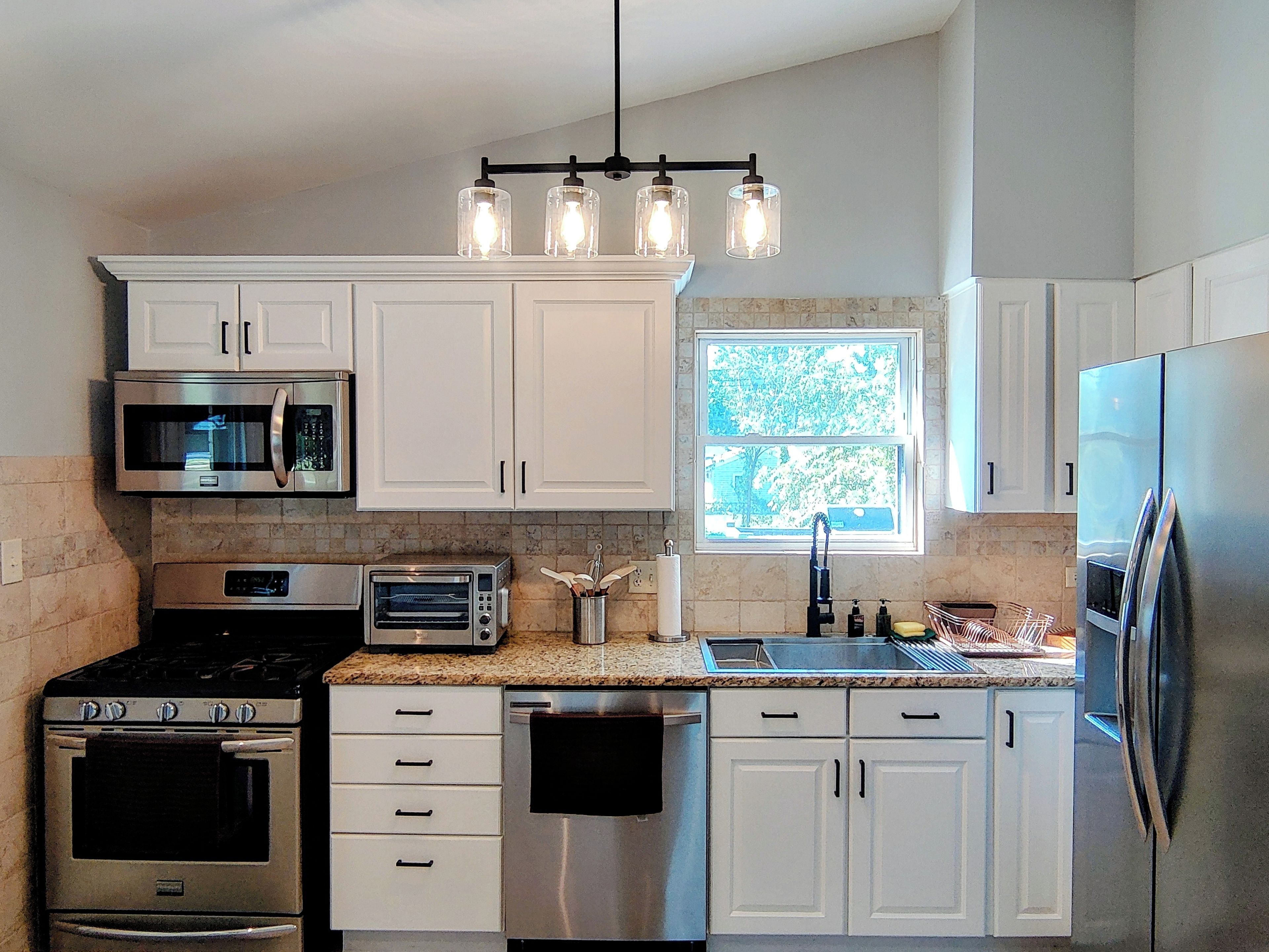 A modern kitchen with white cabinets, stainless steel appliances, a built-in oven, a microwave, a toaster, and a sink.