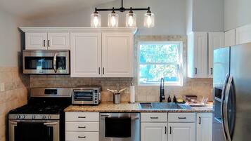 A modern kitchen with white cabinets, stainless steel appliances, a built-in oven, a microwave, a toaster, and a sink.