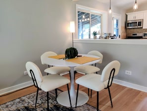 A dining area with a round table, four chairs, a small potted plant, and a window with a view of the outdoors.