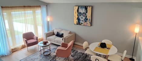 Un salon moderne avec un canapé, des fauteuils, une table basse, un tapis et un tableau accroché au mur.