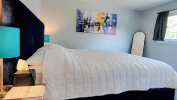 A neatly made bed with a white duvet, a bedside lamp, a book titled 'Sapiens,' and a painting on the wall.