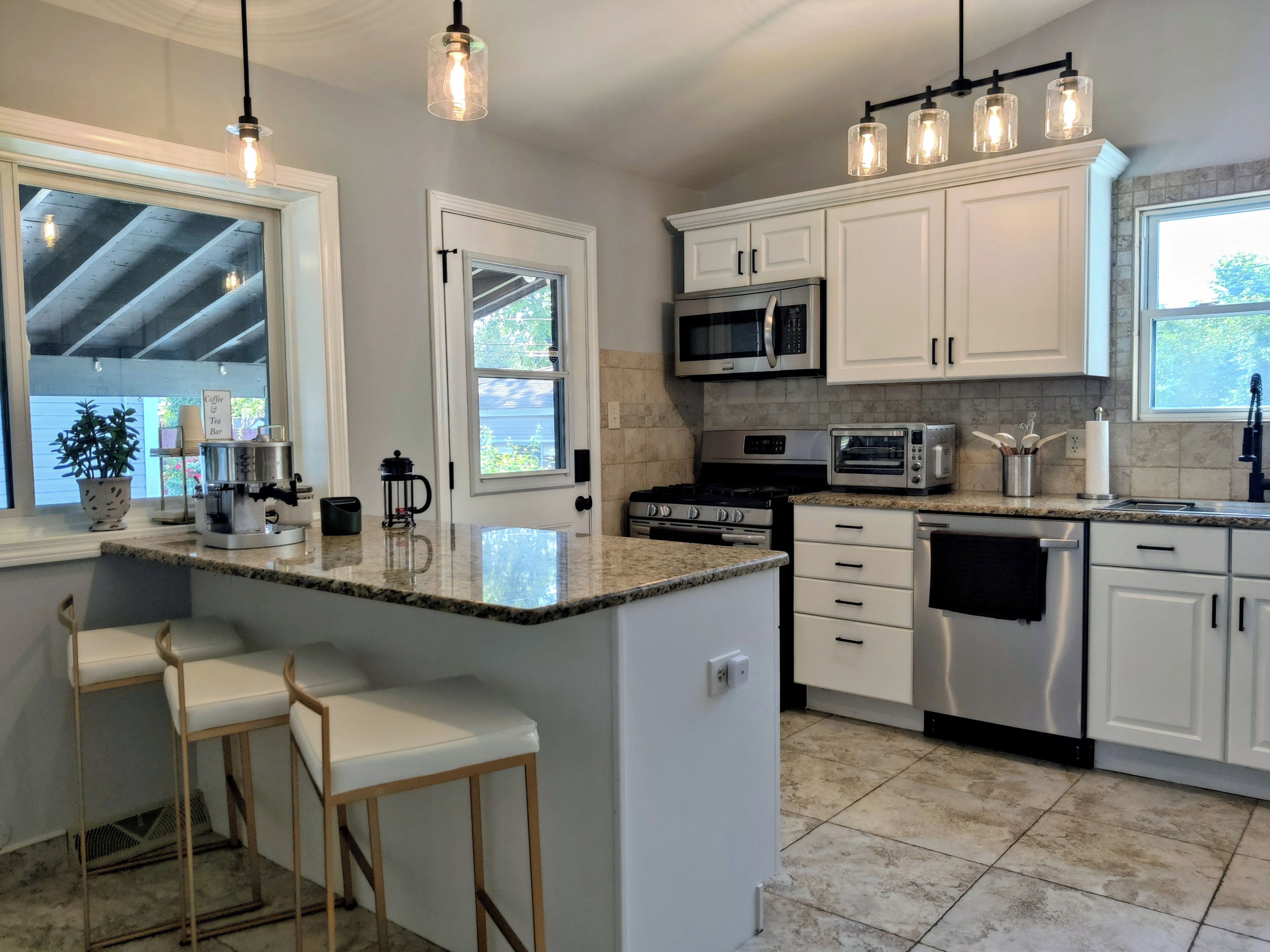 A modern kitchen with white cabinetry, a central island with bar stools, stainless steel appliances, and pendant lighting.