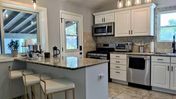 A modern kitchen with white cabinetry, a central island with bar stools, stainless steel appliances, and pendant lighting.