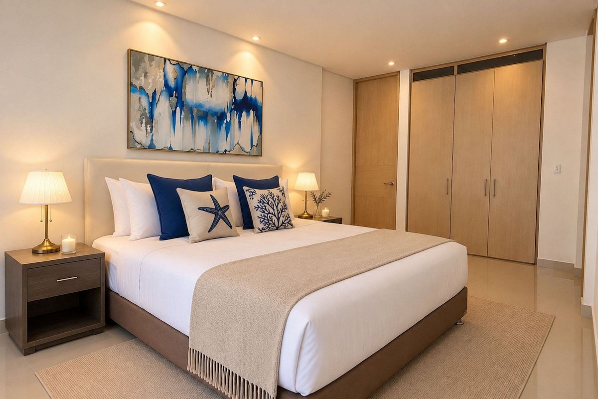 A modern hotel bedroom with a large bed, two bedside tables with lamps, a decorative painting, and a wardrobe.