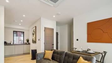 A modern living room with a sofa, a dining table set for two, and a kitchen in the background.