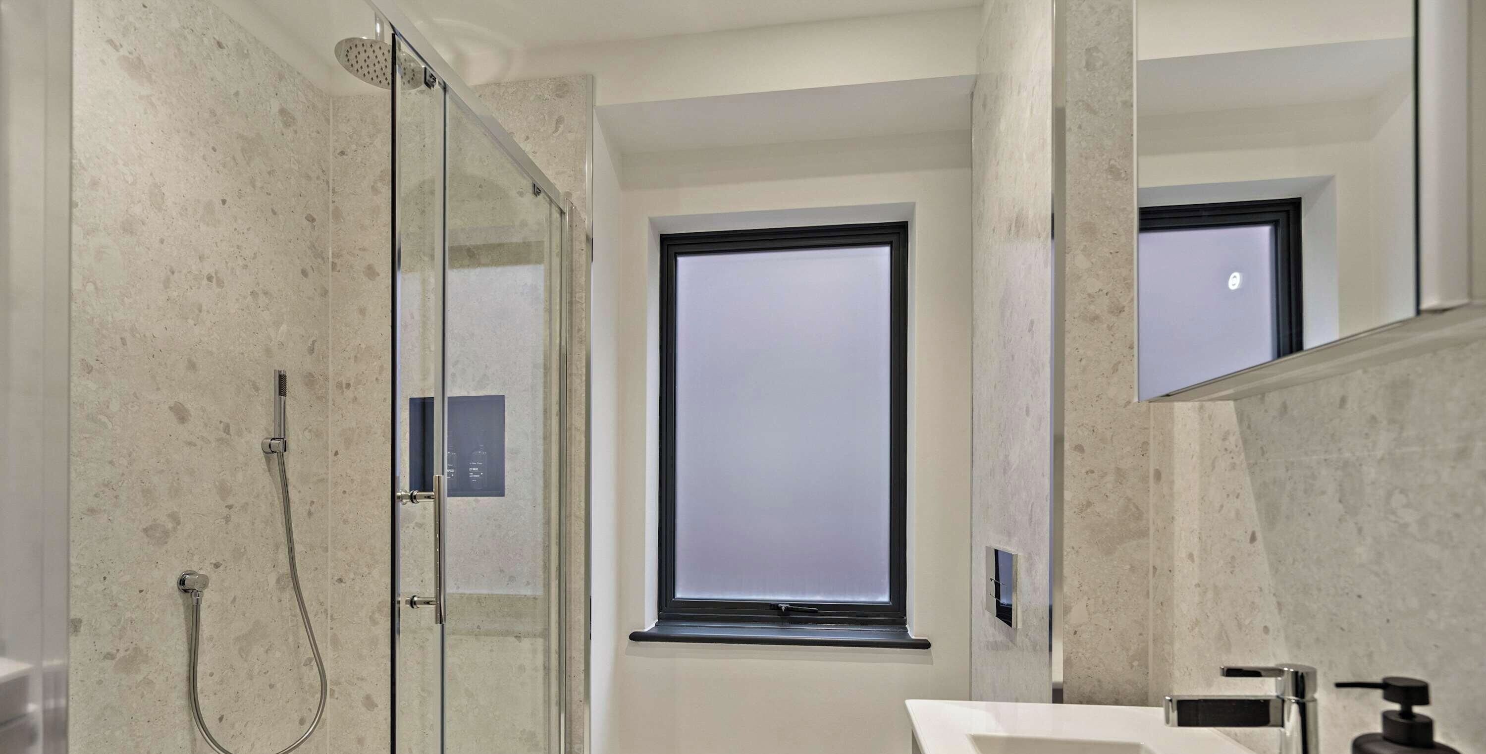 Een moderne badkamer met een douchecabine van glas, een groot raam en een witte wastafel.