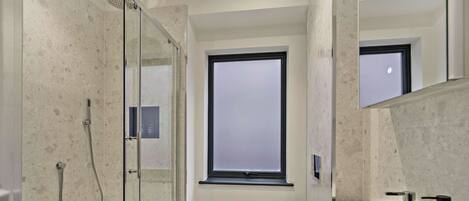 Een moderne badkamer met een douchecabine van glas, een groot raam en een witte wastafel.