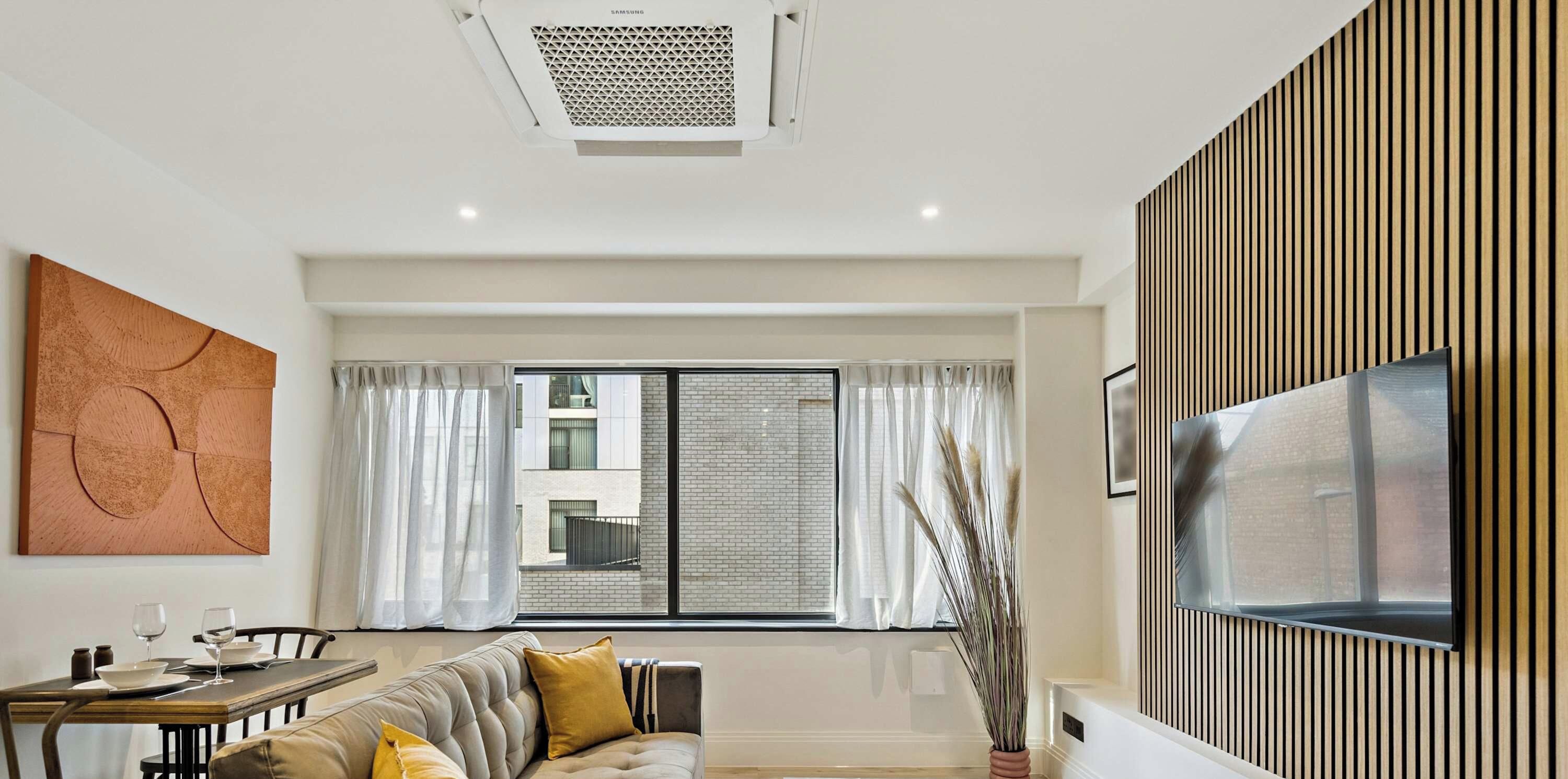 A modern living room with a sofa, dining table, and a TV mounted on a wooden panel wall.