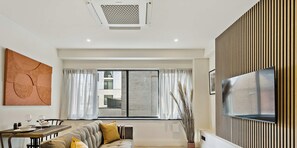 A modern living room with a sofa, dining table, and a TV mounted on a wooden panel wall. - Platform One Apartments - Hexagon (AC THROUGHOUT) (Reading)