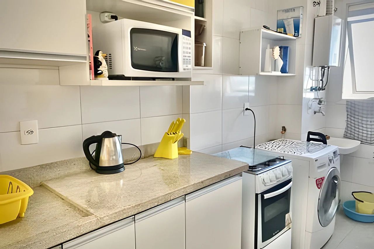 A compact kitchen with a microwave, kettle, and washing machine.