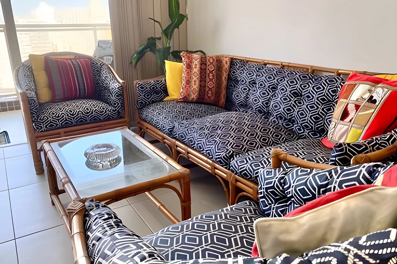 Una sala de estar con una mesa de centro de vidrio, dos sofás estampados y un sillón de mimbre.