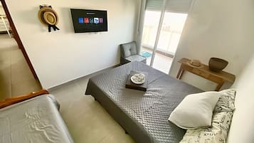 Un dormitorio con una cama, un televisor, una silla y una mesita con un sombrero y un tazón.