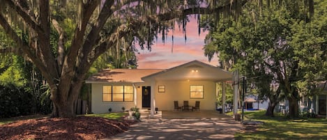 A single-story house with a front porch, surrounded by mature trees with hanging moss.