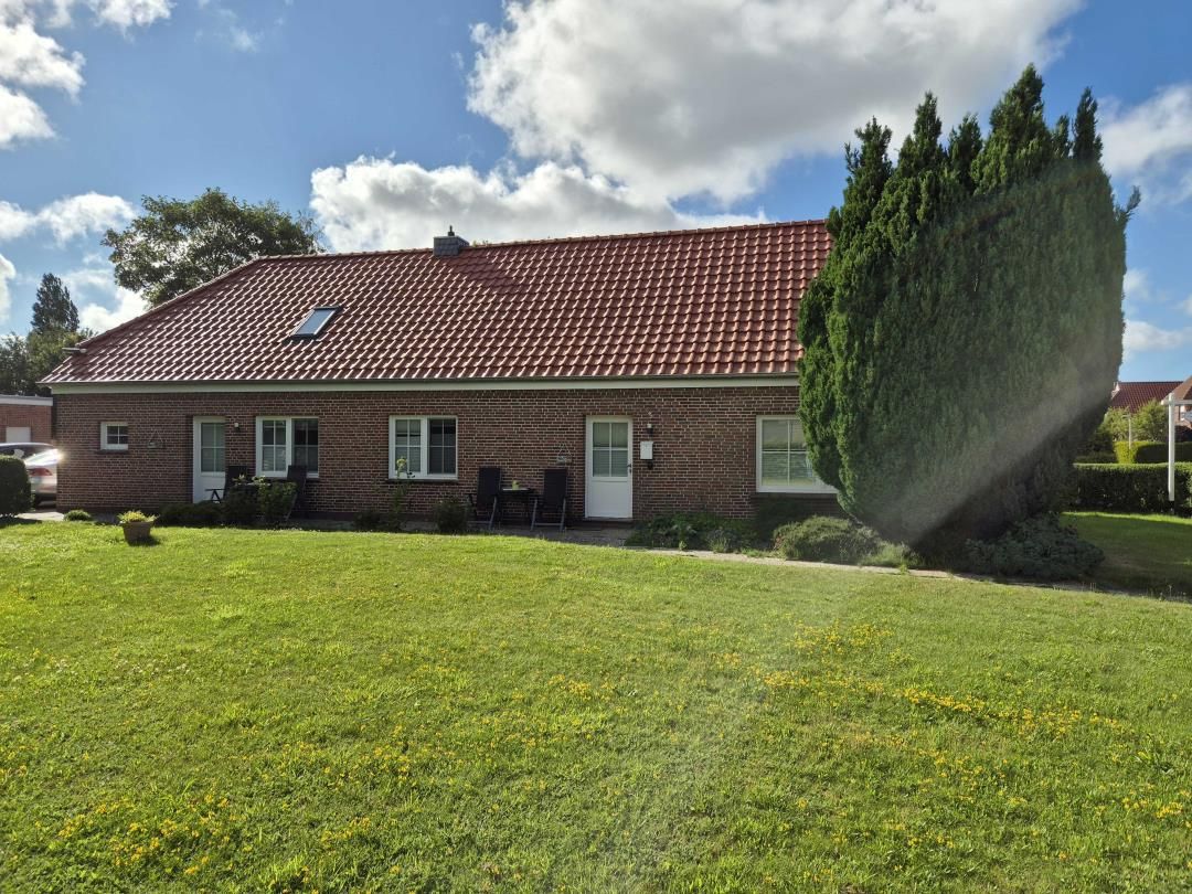 Une maison en briques avec un toit recouvert de tuiles rouges, une pelouse et un grand arbre.
