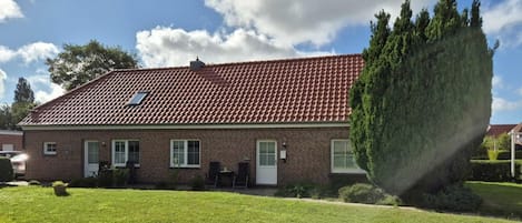 A brick house with a red-tiled roof, a lawn, and a large tree.