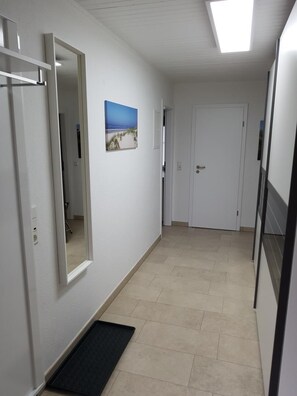Ein Flur mit Tür, einem Spiegel, einem Bild an der Wand und einer Fußmatte im Eingangsbereich.