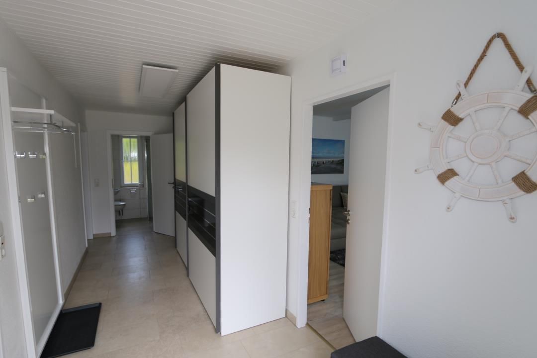 Ein Flur mit einer zur Toilette führenden Tür, einem Kleiderständer und einem an der Wand befestigten dekorativen Gegenstand.