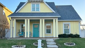 A two-story house with a front porch, a green door, and a small garden area with stepping stones. - Isla Bella - Canal Retreat w Private Dock & Water Views (Port Isabel)