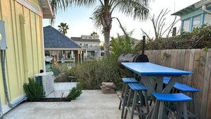 A patio with a concrete floor, a wooden fence, and a blue table with four chairs. - Isla Bella - Canal Retreat w Private Dock & Water Views (Port Isabel)
