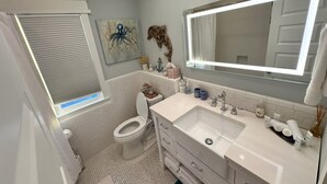 A bathroom with a toilet, sink, and mirror. - Isla Bella - Canal Retreat w Private Dock & Water Views (Port Isabel)