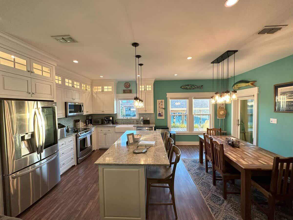 A modern kitchen with stainless steel appliances, a central island, and a dining area with wooden chairs.