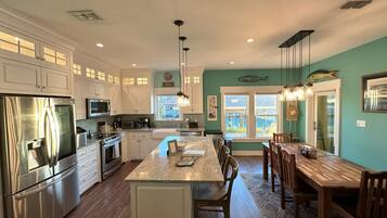 A modern kitchen with stainless steel appliances, a central island, and a dining area with wooden chairs.