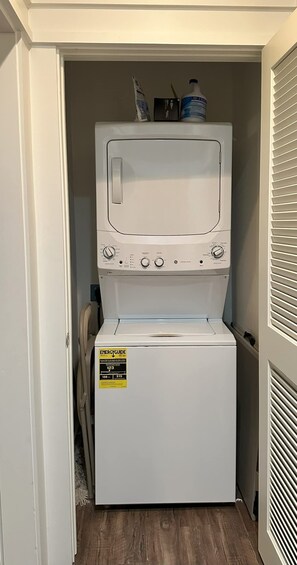 A compact washer and dryer unit in a narrow space with a door on one side and a vent on the other.