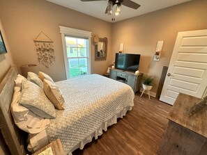 A bedroom with a bed, a TV, a small table with a plant, and a door. - Isla Bella - Canal Retreat w Private Dock & Water Views (Port Isabel)