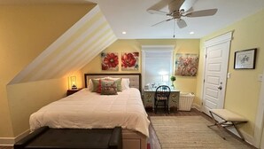 A bedroom with a bed, a desk, a chair, a bench, a ceiling fan, and a door. - Isla Bella - Canal Retreat w Private Dock & Water Views (Port Isabel)