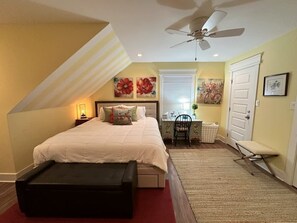 Ein Schlafzimmer mit Bett, Schreibtisch, Stuhl, Bank, Deckenventilator und Tür.