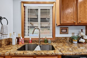Una cocina con un lavaplatos doble, armarios de madera, una ventana con persianas y varios utensilios de cocina sobre la encimera.