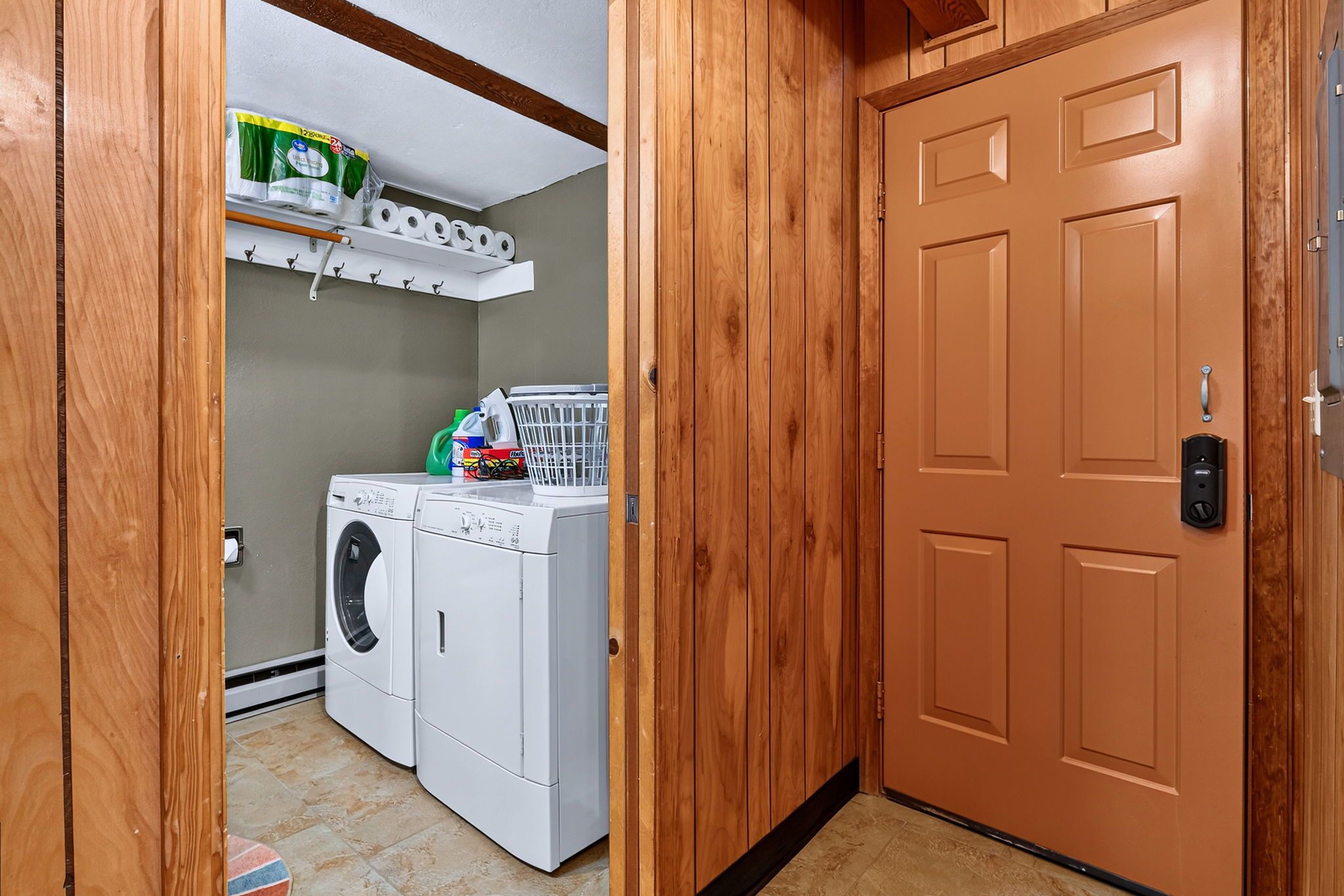Un cuarto de lavandería con lavadora, secadora y repisas con productos de limpieza.