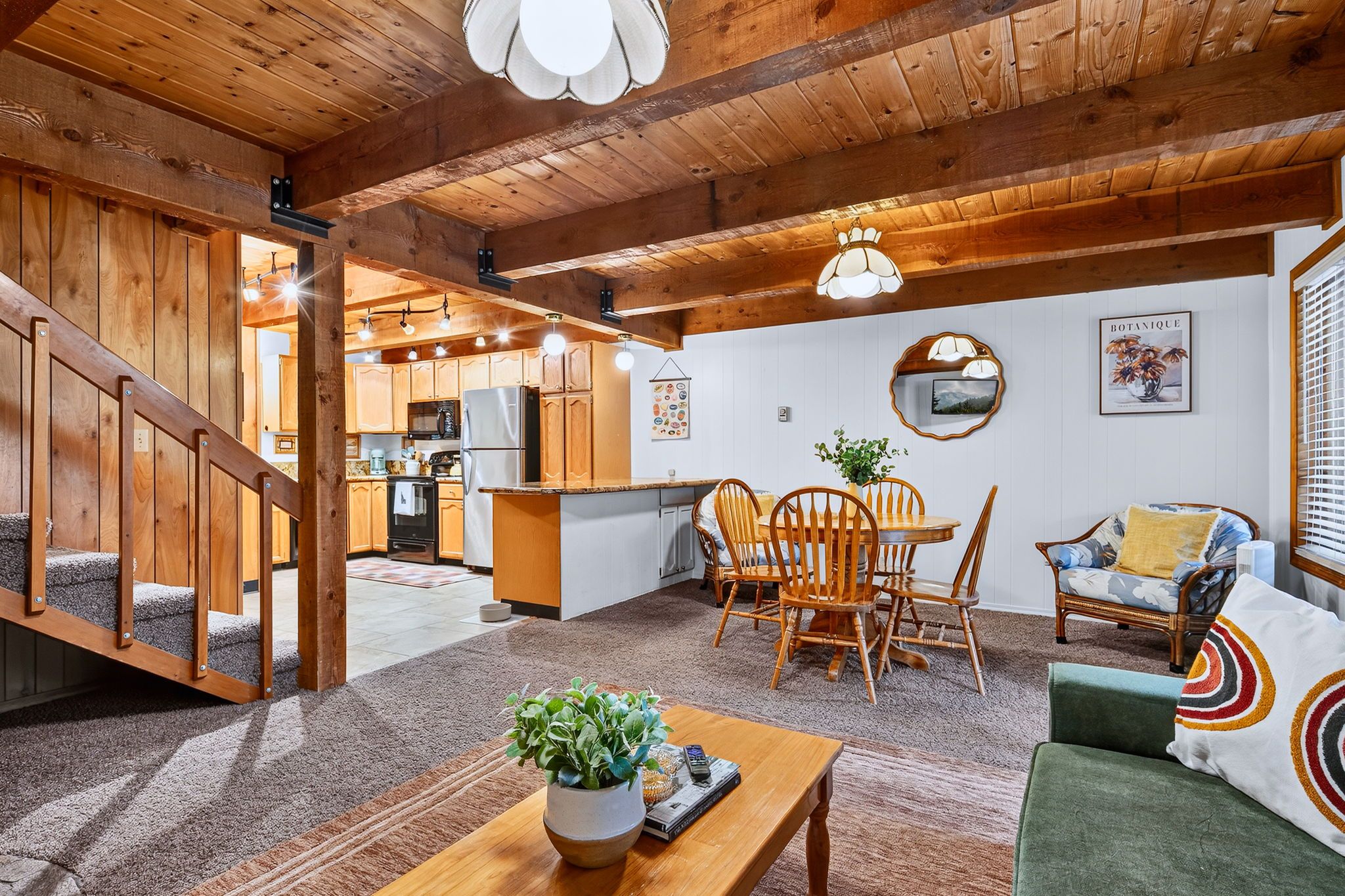 Ein gemütliches Interieur mit einer Holztreppe, einem Essbereich mit Stühlen und einem Tisch sowie einer Küche im Hintergrund.