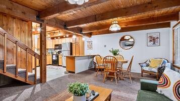 Ein gemütliches Interieur mit einer Holztreppe, einem Essbereich mit Stühlen und einem Tisch sowie einer Küche im Hintergrund.