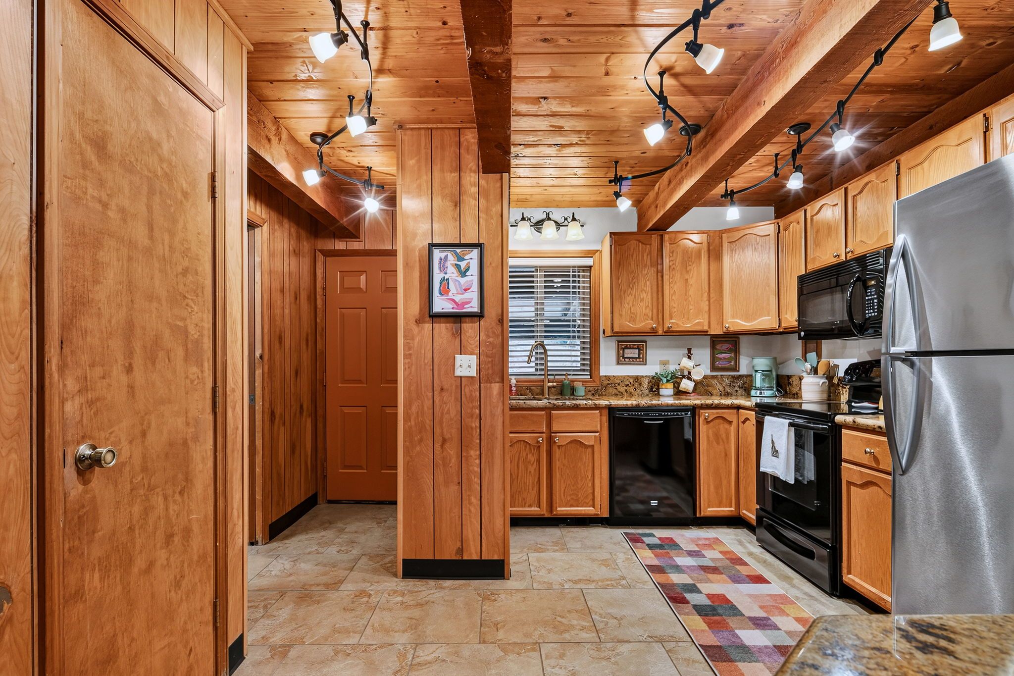 A kitchen with wooden cabinets, a stainless steel refrigerator, and a tiled floor.