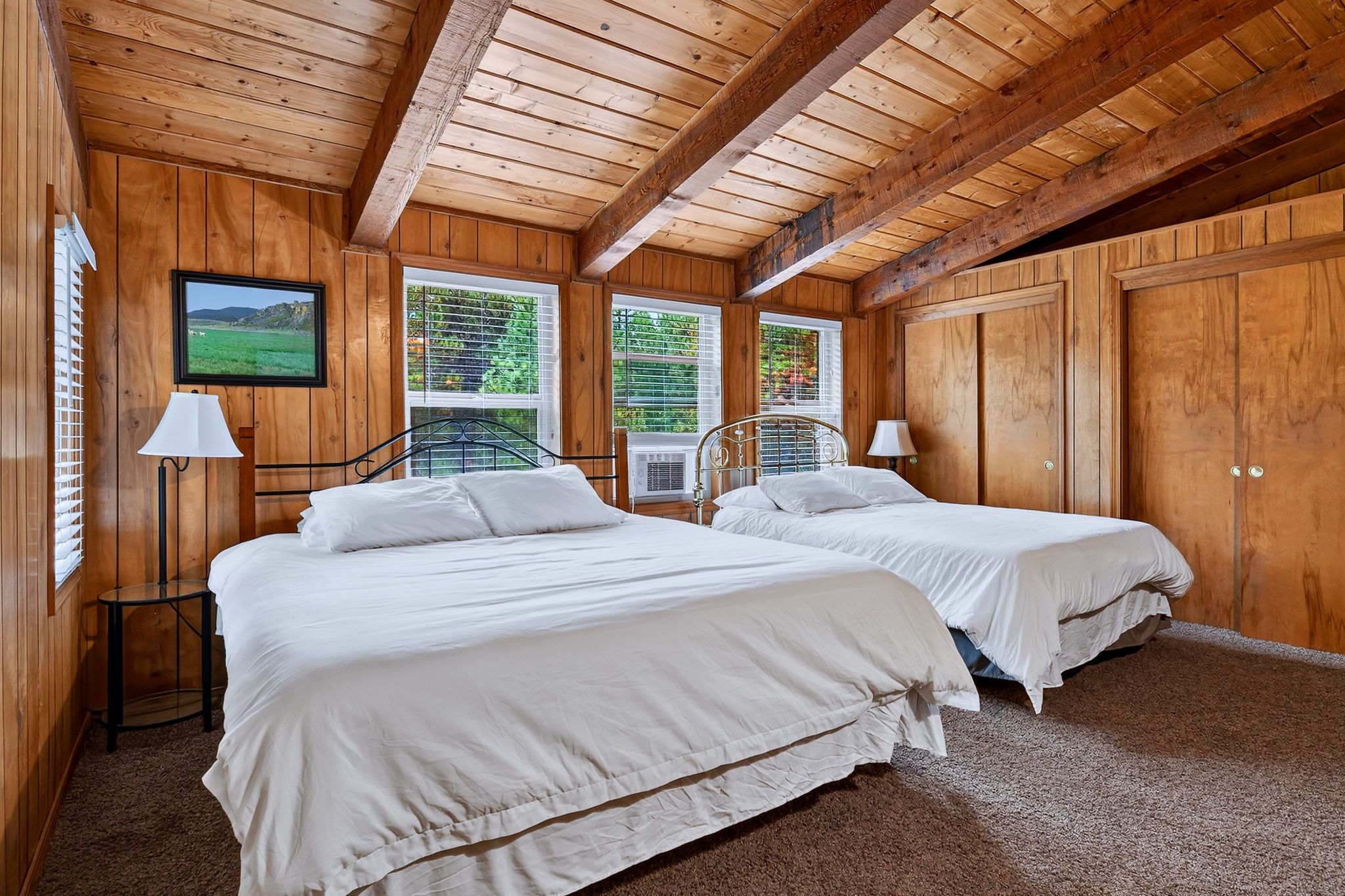 Habitación con dos camas, paredes de madera, un cuadro en la pared y ventanas con persianas.