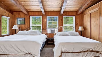 A room with two beds, wooden walls, and a window with blinds.