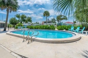 A swimming pool with a metal ladder, surrounded by green plants and blue chairs.