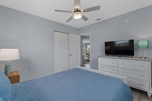 A bedroom with a bed, a television, a dresser, a lamp, and a ceiling fan.